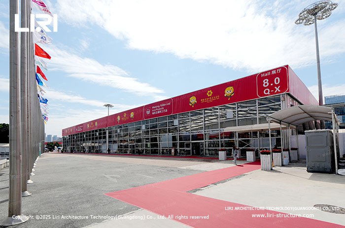 Large exhibition hall tent exterior with flagpoles and red carpet entrance