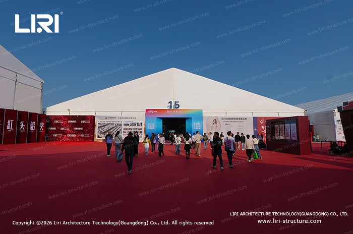 Large exhibition tent entrance with visitors walking in on red carpet
